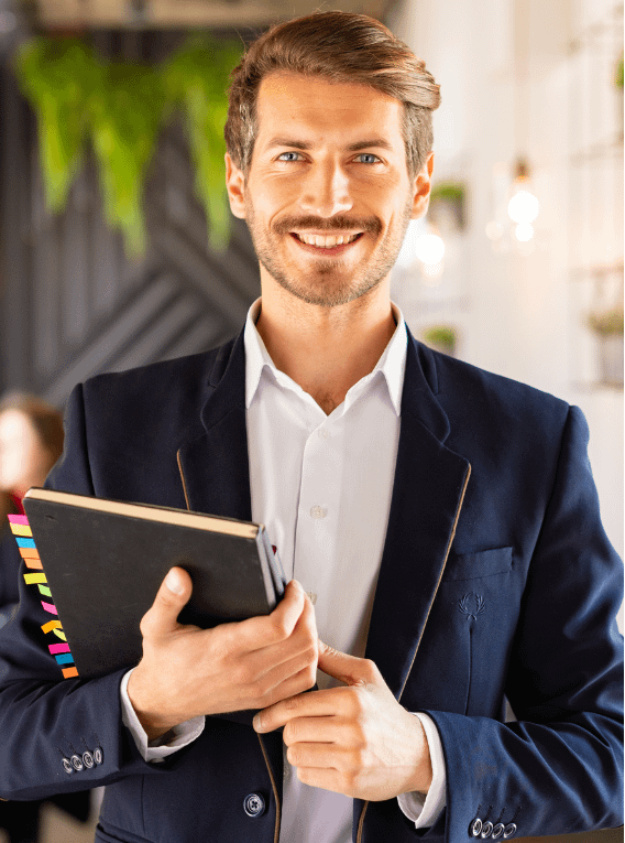 A confidently smiling professional individual holding a notebook in an office environment