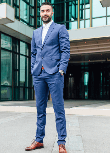 A professional individual in a tailored blue suit stands confidently outside a modern building, symbolizing the poise and assurance of diplomats.